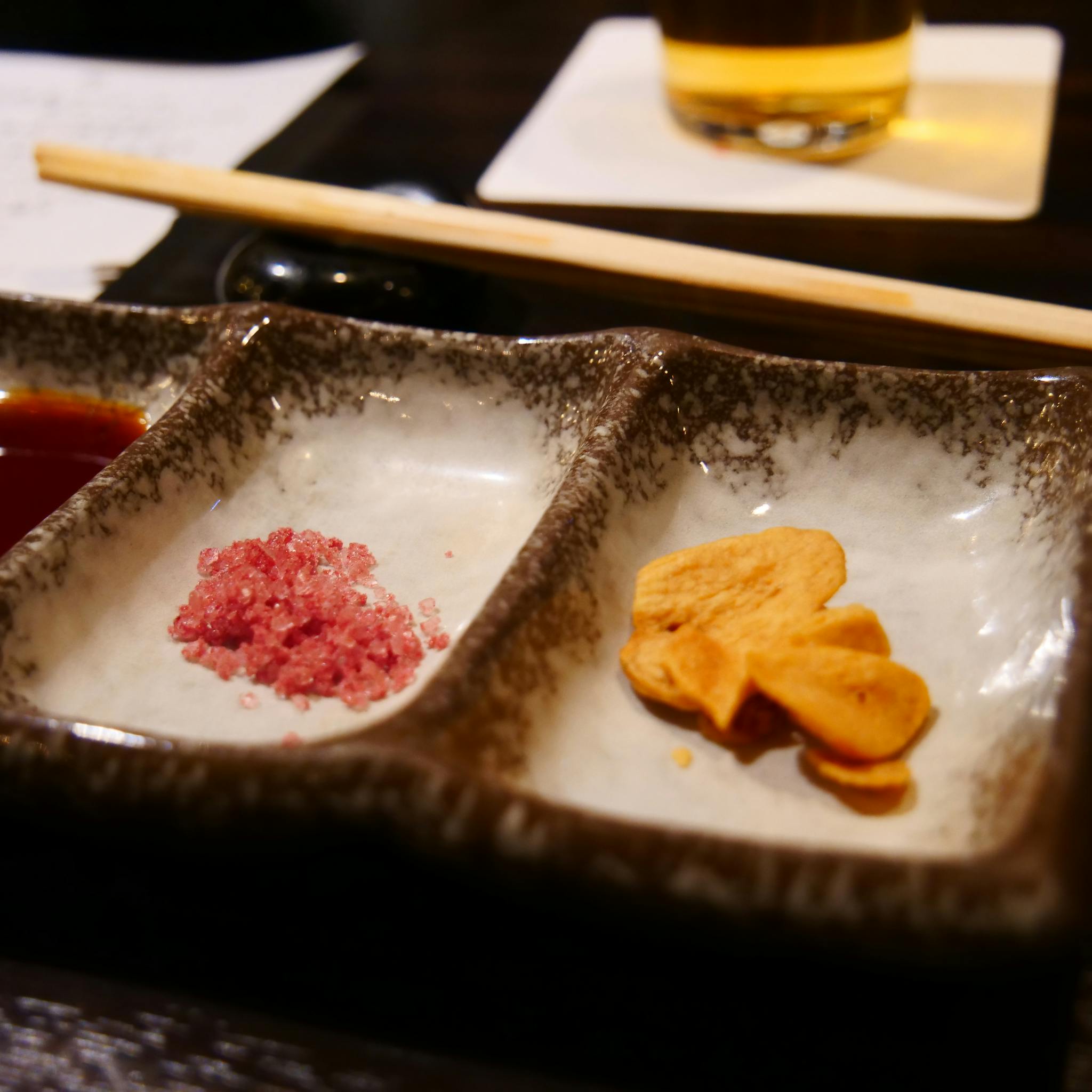 Elegant dining setup featuring a trisection dish with rock salt, pickles, and soy sauce in a restaurant setting.