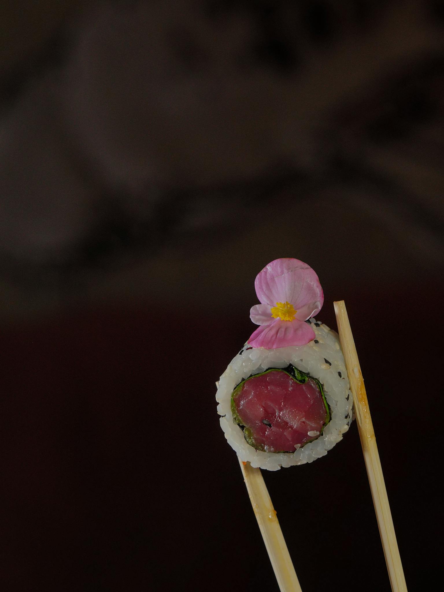 Elegant sushi roll with flower, held by chopsticks, showcasing Japanese culinary art.